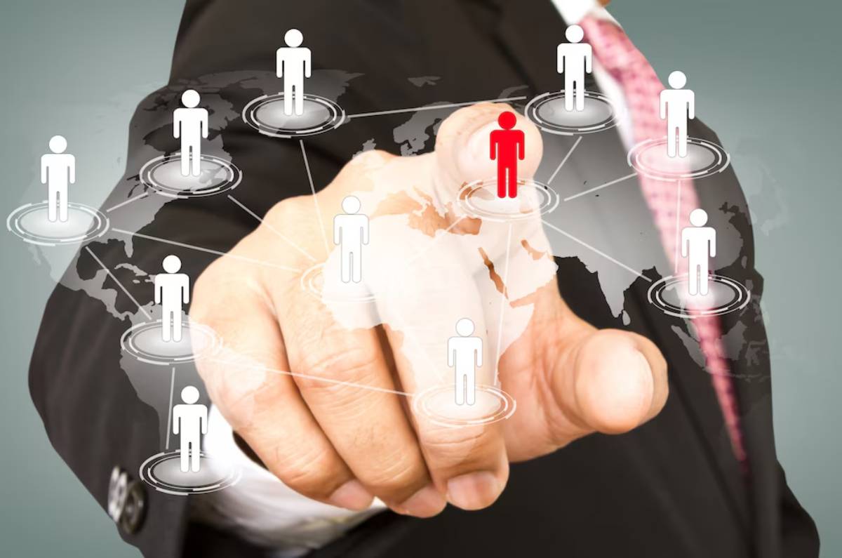 A businessman points at digital icons representing people on a world map interface, highlighting global connectivity and management.