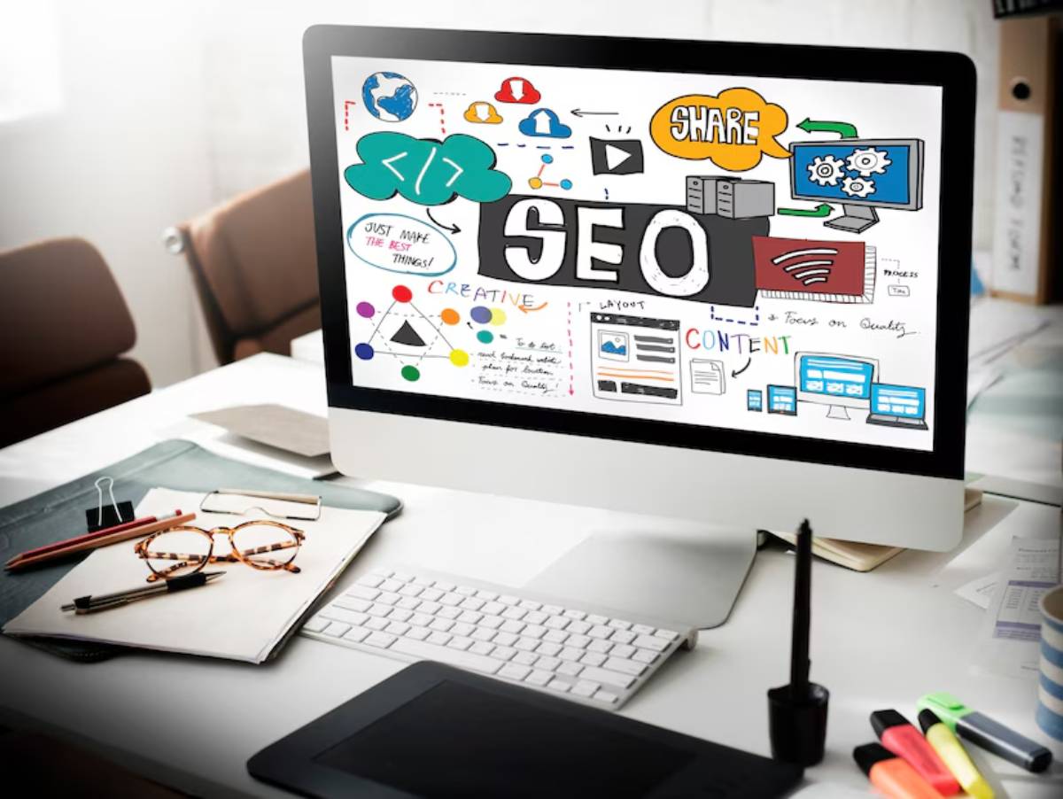 Computer screen displaying colorful SEO and content-related graphics, on a desk with glasses, pens, and notes.