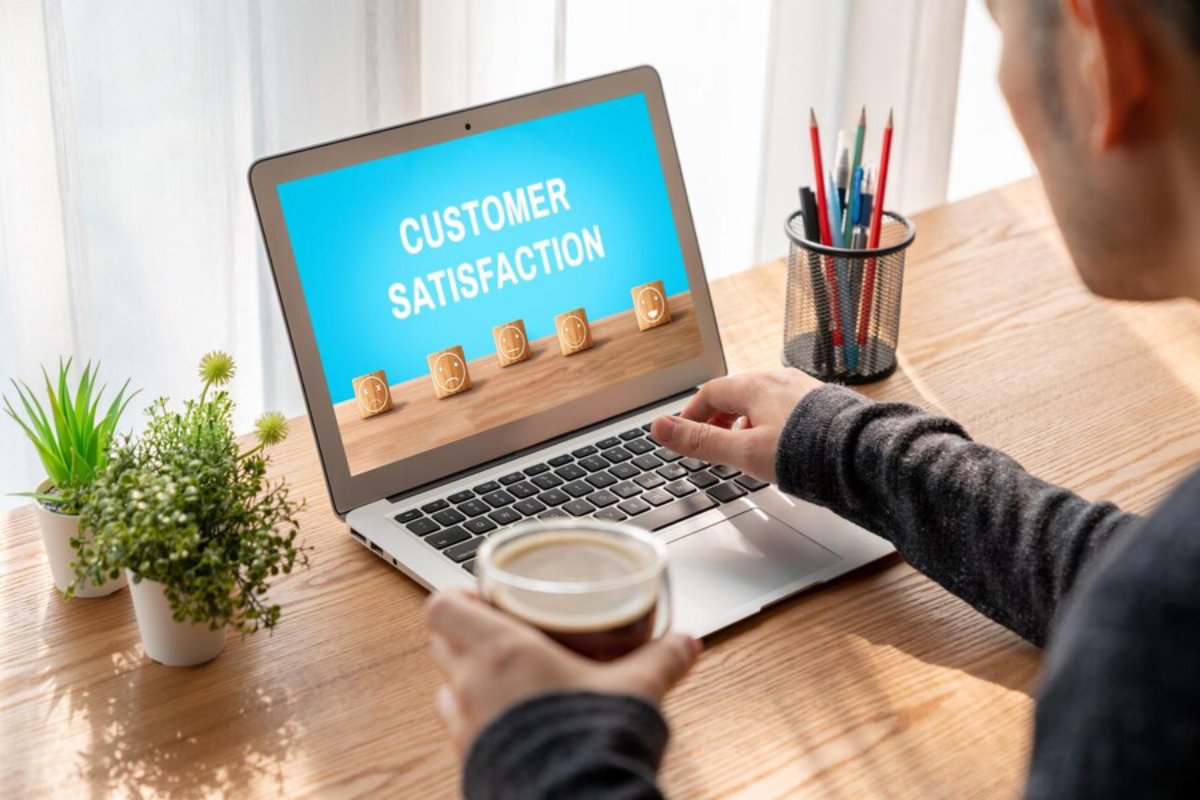 Person using a laptop displaying Customer Satisfaction with five-star rating, holding a coffee cup.