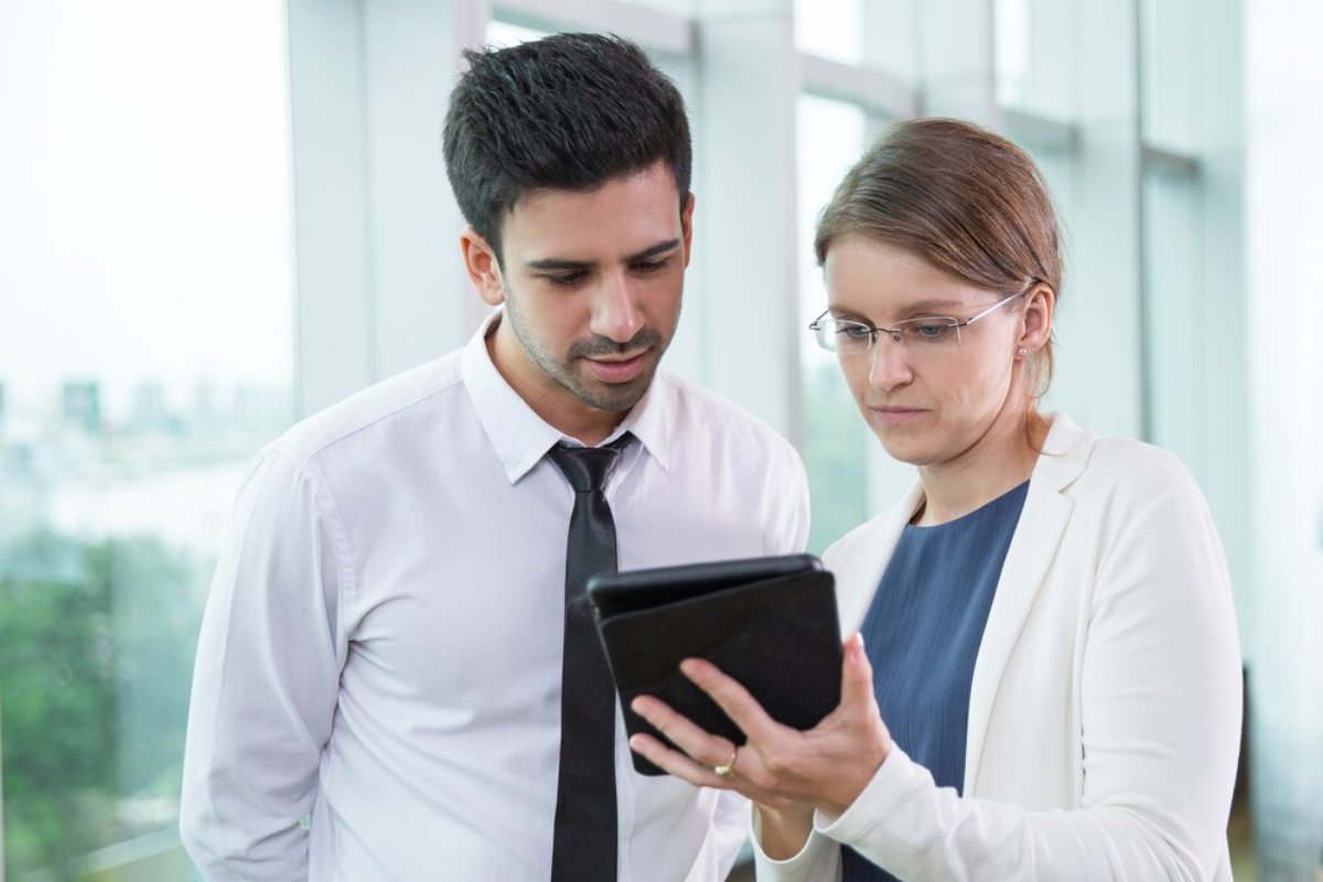 Two professionals, a man and a woman, examining a tablet together in a modern office setting.