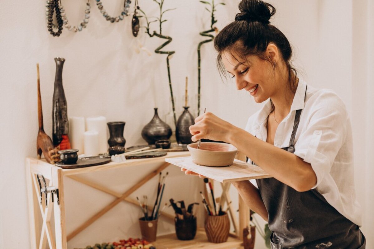 A woman enjoys painting in a pottery workshop surrounded by crafted pottery and artistic tools.