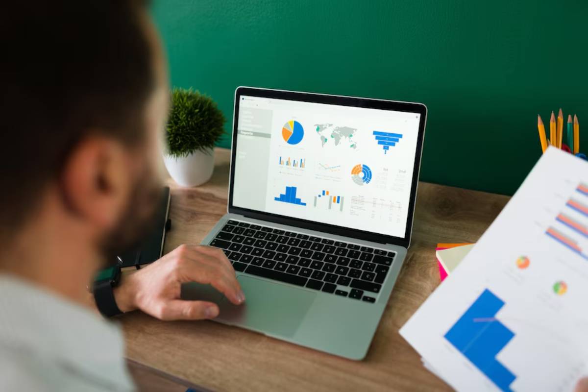 Man analyzing financial data on a laptop with graphs and charts displayed on the screen in an office setting.
