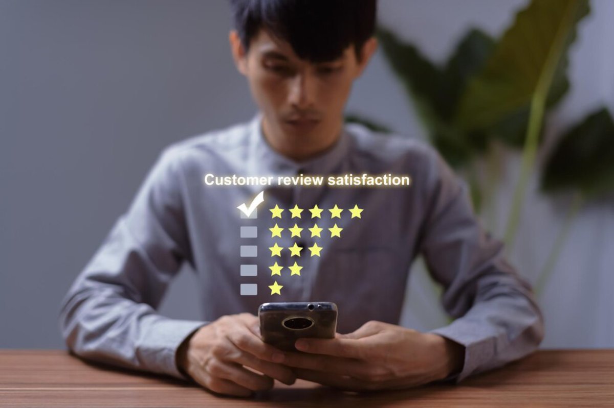 Young man at a table using a smartphone with a digital customer review satisfaction rating displayed above it.