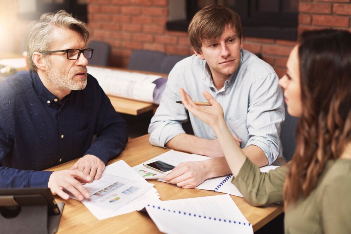 Three professionals discussing over documents in a well-lit, casual office setting.