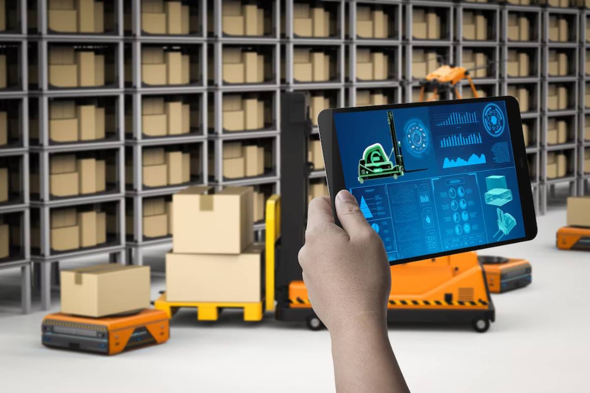 Person holding a tablet with logistics graphics, in a warehouse with automated robots and shelves filled with boxes.