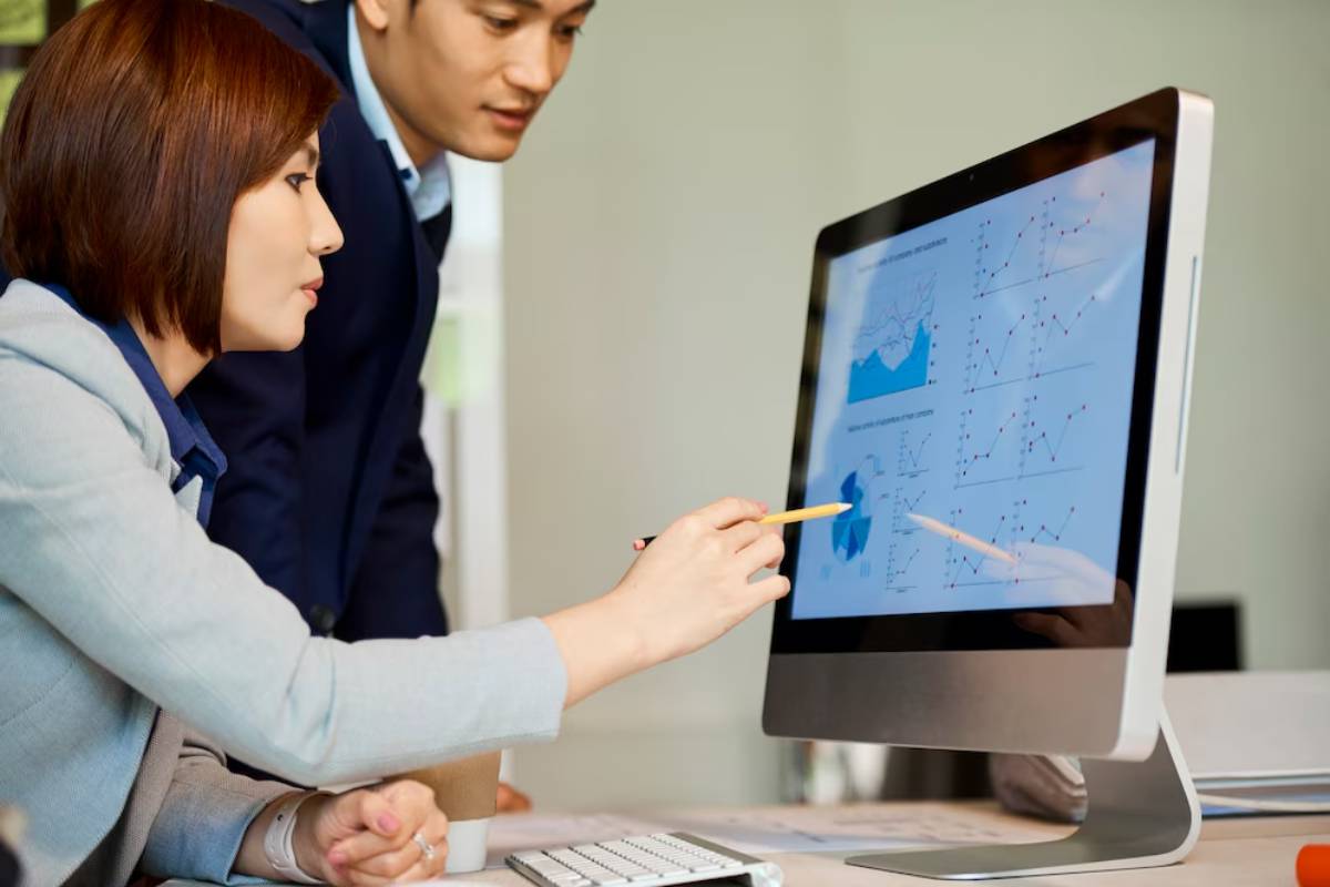 Two professionals analyzing data graphs on a computer screen in an office setting.