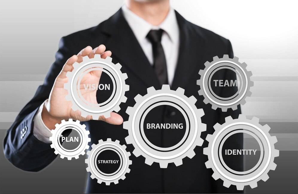 Businessman in a suit interacting with floating gears labeled with business concepts like Vision, Plan, Strategy, Branding, Team, and Identity.