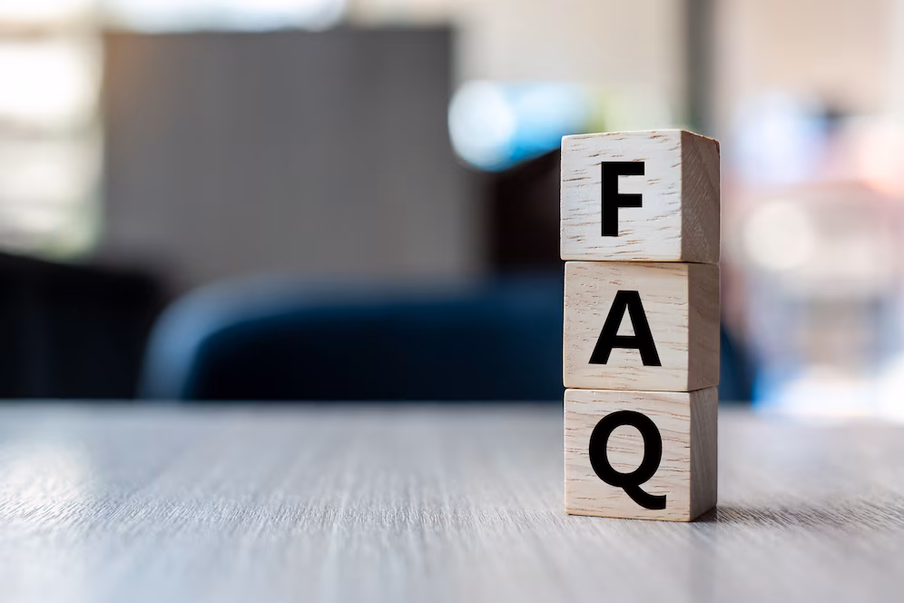 Wooden blocks stacked to spell FAQ on a table with a blurred office background.