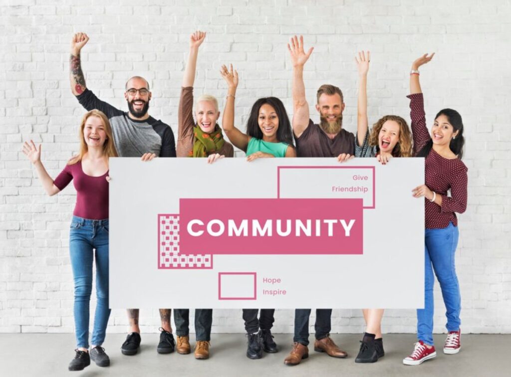 Diverse group of joyful people holding a sign that reads COMMUNITY against a white brick wall.