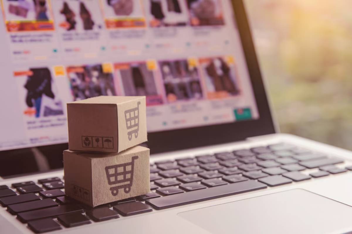 Cardboard boxes with shopping cart icons on a laptop keyboard, indicating online shopping.