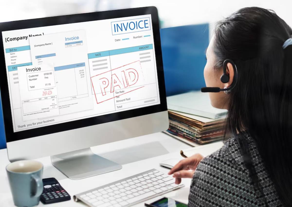 Woman with headset reviewing a digital PAID invoice on a computer screen.