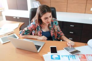 Woman analyzing financial charts with calculator and laptop on office desk.