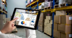 Person pointing at a warehouse management dashboard on a tablet in a storeroom.