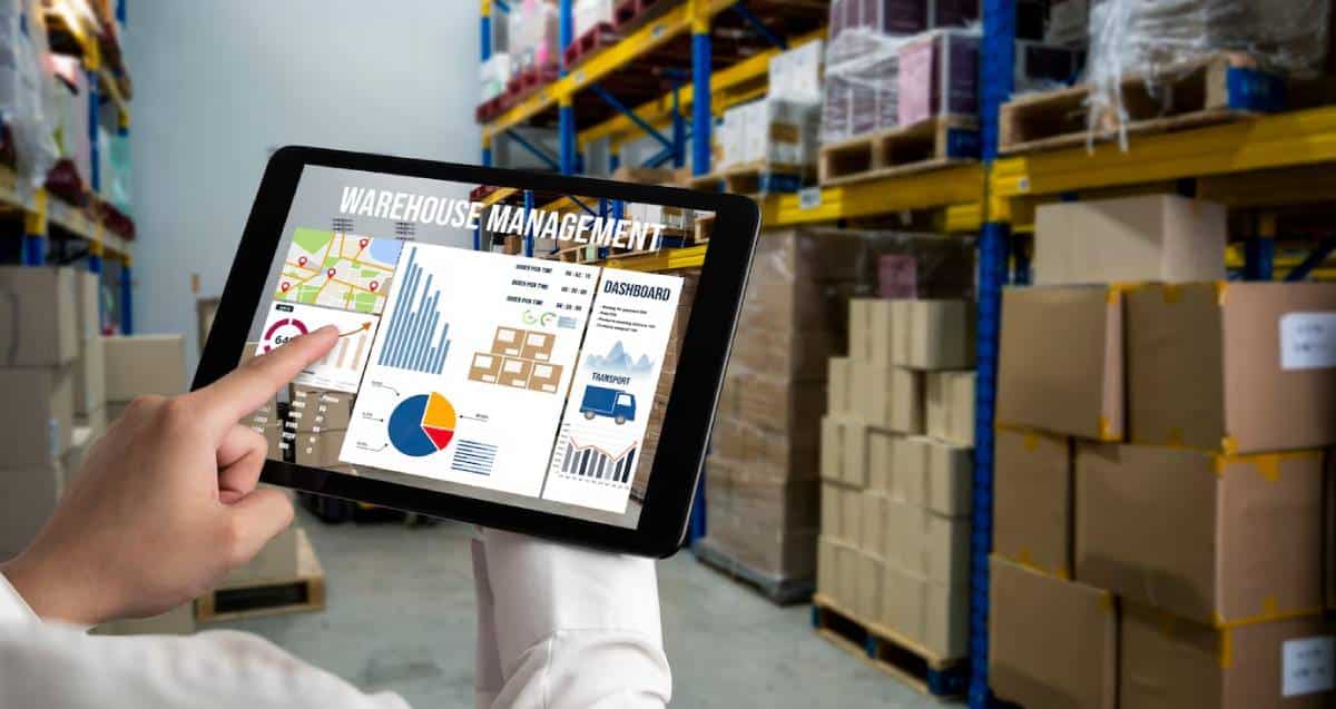 Person pointing at a warehouse management dashboard on a tablet in a storeroom.