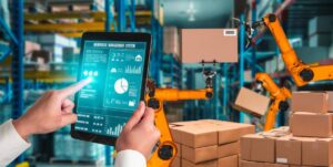 Person using a digital tablet to manage robotic arms in a warehouse setting.