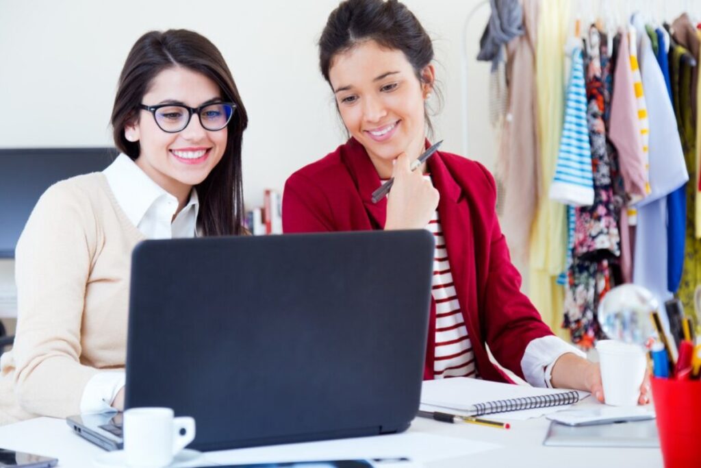Two women smiling and working together on a laptop in a colorful office space.