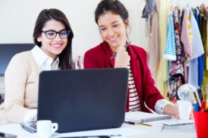 Two women smiling and working together on a laptop in a colorful office space.