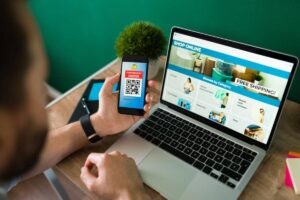 Man scans QR code on phone for a discount, with online shopping site open on laptop.
